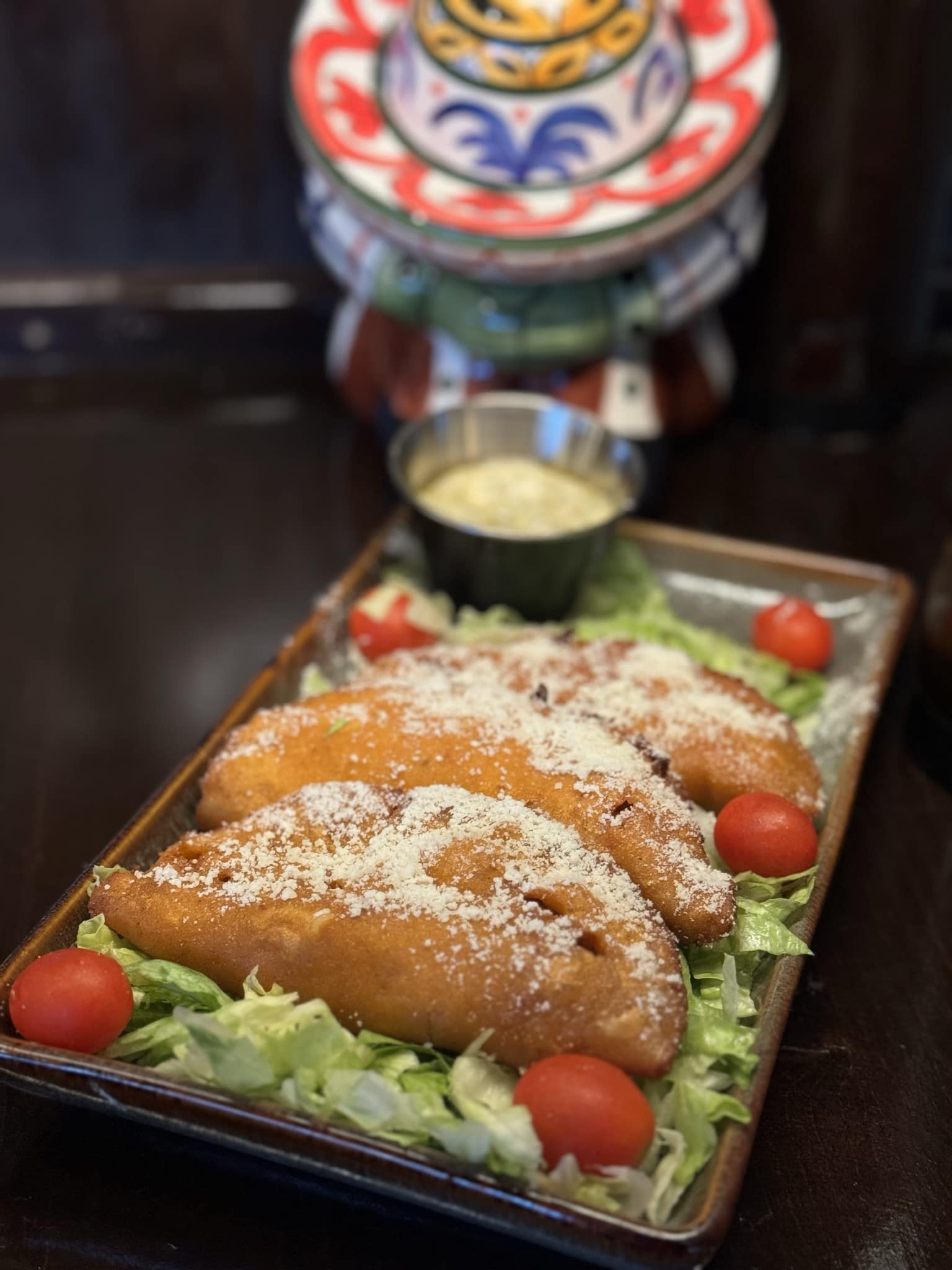 A plate of three golden-brown empanadas topped with grated cheese and served with a side of lettuce and cherry tomatoes.