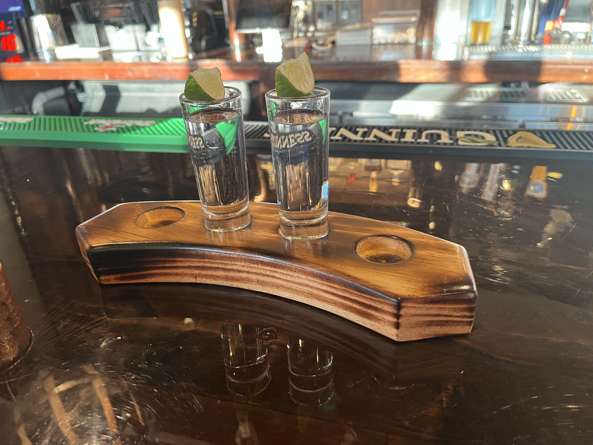 Two shot glasses of tequila on a wooden holder with lime wedges.